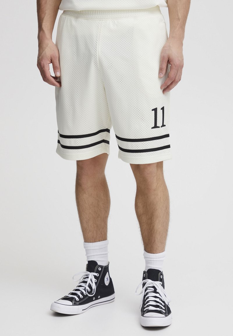 Hvide mesh basketballshorts med sorte striber ved kanten og nummer 11 på venstre ben. Båret med sorte hightop sneakers og hvide sokker.