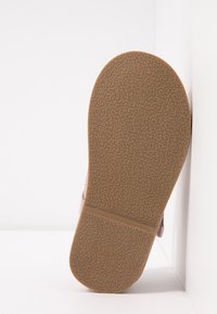 Gumowa podeszwa buta, z teksturowaną brązową powierzchnią i delikatnie zaokrąglonym kształtem, z różową cholewką widoczną z boku.