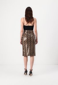 Jupe crayon en imprimé serpent marron avec une taille haute et une texture brillante, associée à un haut noir ajusté et des escarpins noirs à talons aiguilles.