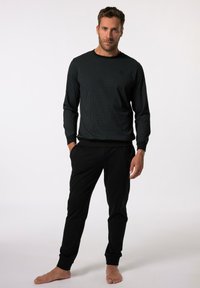 Camisa negra de manga larga con cuello redondo, combinada con pantalones ajustados negros. El atuendo cuenta con puños ceñidos y un corte relajado.