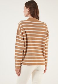 Pulover rayat de culoare bej cu dungi orizontale albe, având o croială lejeră, mâneci lungi și gât rotund. Textură moale din tricot.