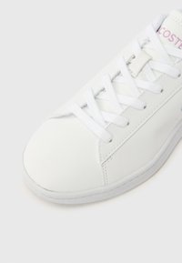 Λευκό αθλητικό παπούτσι με λείο δερμάτινο επάνω μέρος, στρογγυλεμένη μύτη και επίπεδα κορδόνια. Διαθέτει διακριτική ραφή και λογότυπο σε ροζ χρώμα στο πλάι.