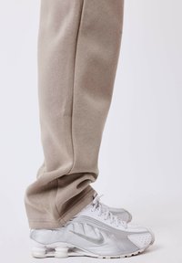 Beige loose-fitting sweatpants paired with white and silver Nike sneakers featuring perforated details and a prominent logo on the side.