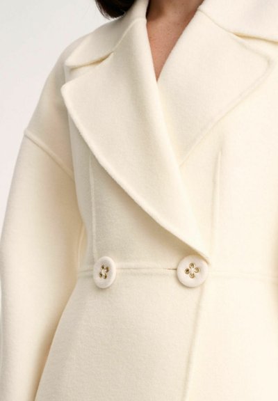 Cream wool blend coat featuring a double-breasted design, large lapels, and decorative buttons with floral accents. Smooth texture.