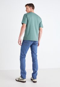 Camiseta de algodón color verde azulado, de cuello redondo y mangas cortas, combinada con jeans de mezclilla azul. Los zapatos son de color verde claro con acentos oscuros y una suela estampada.