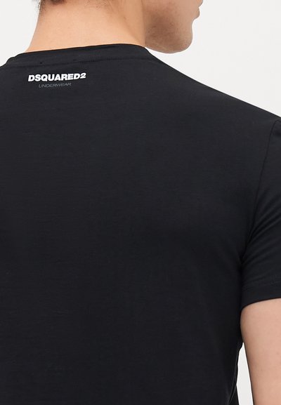 Muškarac nosi crnu majicu s bijelim logotipom "DSQUARED2 UNDERWEAR" otisnutim na gornjem dijelu leđa.