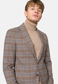 Brązowa marynarka w kratę z niebieskimi i białymi akcentami, usztywniony fason, zapięcie na jeden guzik, noszona na beżowym swetrze z golfem.