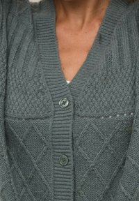Green knitted cardigan with a V-neck, featuring diamond and ribbed patterns, finished with two green buttons. Soft texture.