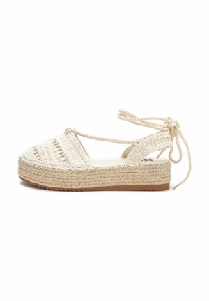 Sandal de cuña de esparto en color beige con parte superior tejida, lazos en el tobillo y suela texturizada. Cuenta con un diseño de cuerda trenzada y suela de goma plana.