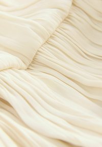 Tessuto color crema con pieghe orizzontali strette che creano morbide e uniformi pieghe e texture sulla superficie.