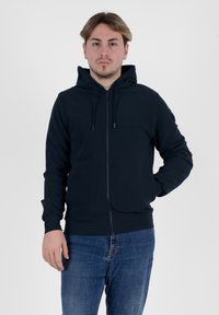 Felpa con zip di colore navy, dotata di cappuccio regolabile con cordino, polsini e vita a coste. Realizzata in tessuto morbido, abbinata a jeans in denim blu. Design semplice.
