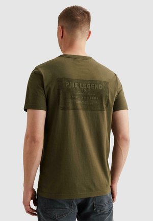 Mann trägt ein olivgrünes kurzärmeliges T-Shirt mit verblasstem schwarzem rechteckigem Logo und dem Text "PME Legend Co Finest Cargo Goods" auf dem Rücken.