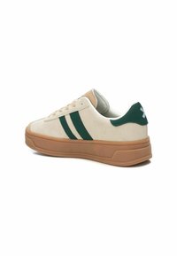 Zapatillas de ante beige con rayas verdes y suela de goma marrón. Presentan un collar acolchado y un diseño de laceado texturizado.