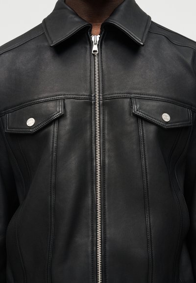 Κοντινό πλάνο ατόμου που φοράει μαύρο δερμάτινο μπουφάν με ασημένιο φερμουάρ και τσεπάκια στο στήθος με κουμπιά, κολάρο ορατό.