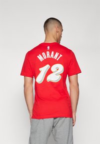 T-shirt en coton rouge avec le nom "MORANT" et le numéro "12" en grandes lettres blanches et dorées au dos.
