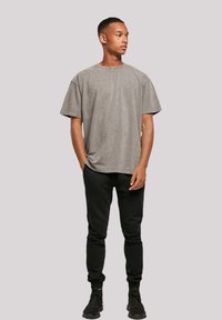 Graues, übergroßes T-Shirt mit Rundhalsausschnitt und kurzen Ärmeln, kombiniert mit schwarzen, eng anliegenden Jogginghosen und schwarzen Sneakern. Glatte Textur, lässiges Design.