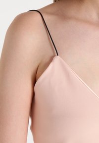Ljus rosa camisole med tunna svarta spaghettistillar, med en slät textur och en V-ringning som framhäver en figurnära silhuett.