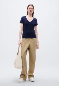 Μπλε μπλουζάκι με V λαιμόκοψη, άνετη εφαρμογή, σε συνδυασμό με μπεζ παντελόνι με φαρδιά πόδια και λευκά παπούτσια. Το μοντέλο κρατάει μια κρεμ τσάντα. Απλός σχεδιασμός, απαλή υφή.