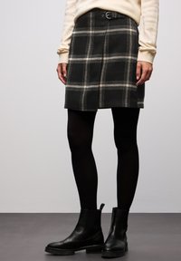 Wollen geruite rok in donkergrijs met witte lijnen, met een aangesloten taille en riemlussen, gecombineerd met zwarte maillots en enkellaarsjes.