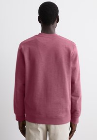 Roosa pullover-sviiter, mis on valmistatud pehmest kangast, pika varrukaga ning ribaga kaeluse ja mansettidega.