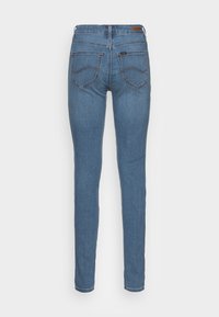 Jeans ajustados de talle medio en denim azul claro, con dos bolsillos traseros, costuras sutiles y una etiqueta de cuero en la cinturilla.