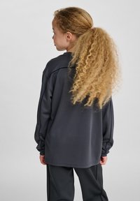 Mörkgrå sweatshirt med långa ärmar, rund hals och avslappnad passform, kombinerad med matchande byxor. Lockigt hår satt upp.