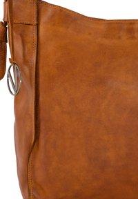 Braune Leder-Tote mit glatter Textur, die ein silbernes, rundes Hardware-Detail aufweist. Einfaches Design und großzügige Struktur.