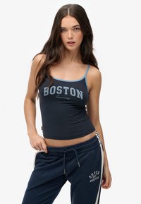 Navy tanktop met lichtblauwe schouderbanden en "BOSTON" tekst in het grijs gedrukt. Een paar bijpassende marineblauwe sweatpants met witte zijstrepen en logo.