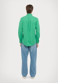 Zelená košile s dlouhým rukávem, rovný lem, zapínání na knoflíky a detaily na švech ramen, spárovaná s volnými světle modrými džíny.