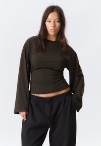 Maglia a maniche lunghe color oliva scuro con bustino aderente e maniche larghe, abbinata a pantaloni neri con vita elastica. Tessuto dalla trama liscia.