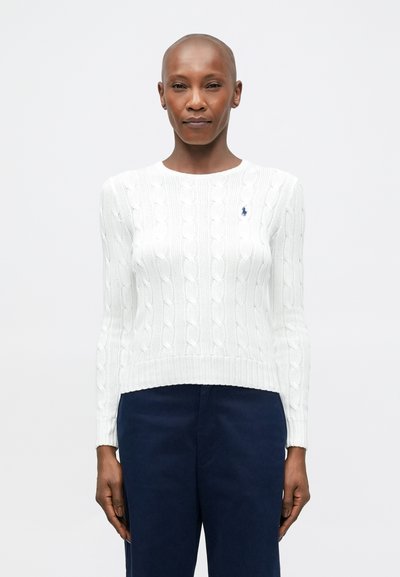 Maglione bianco a maglia a treccia con orlo a coste, maniche lunghe e un piccolo logo blu sul petto. Abbinato a pantaloni blu scuro.