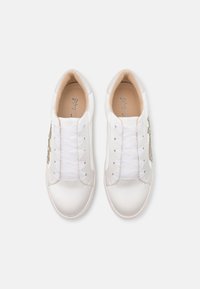 White sneakers with a smooth synthetic upper, featuring white laces, a light-colored insole, and a decorative gold accent on the side.