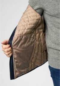 Giacca trapuntata in stile puffer con esterno blu navy e interno beige. Presenta una texture satinata e una tasca interna.