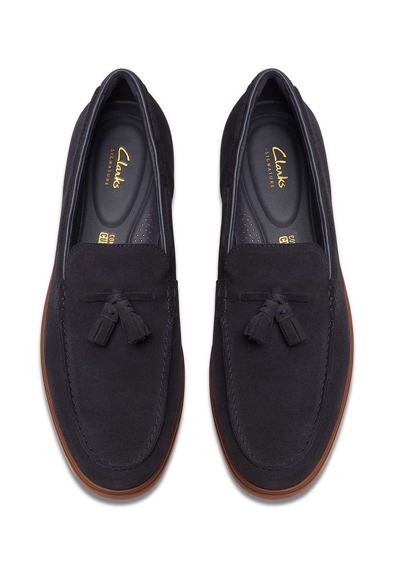 Granatowe zamszowe mokasyny o gładkiej fakturze, z ozdobnym chwostem i kontrastującą brązową gumową podeszwą. Wnętrze z marki Clarks Signature.