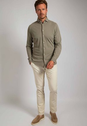 Licht olijfgroen shirt met knopen, lange mouwen, gladde structuur, gecombineerd met crèmekleurige broek en bruine instappers. Eenvoudig ontwerp en getailleerde vorm.