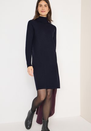 Robe turtleneck bleu marine à manches longues. Fabriquée en tissu texturé, elle présente une coupe droite. Portée avec des bottes de combat noires et des collants transparents.