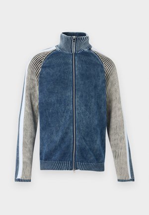 Adīta zilā rāvējslēdzēja jaka ar ribveida apkakli, ar kontrastējošām pelēkām un baltām svītrainām piedurknēm un teksturētu apdari.