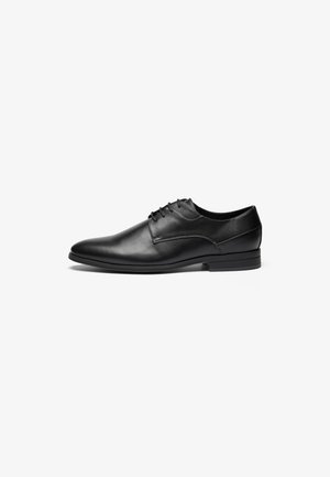 Chaussure de ville en cuir noir avec une texture lisse, bout rond et un design à lacets à quatre œillets. Elle présente un talon bas empilé et des détails cousus.