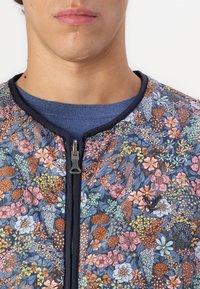 Floral zip-up jacket featuring a navy background with multicolored flower patterns, smooth fabric, and a black zipper closure.