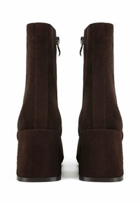 Bottines en suède marron avec un talon carré, fermeture à glissière et texture lisse. Des détails cousus courent verticalement le long des côtés.