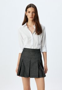 Camisa de cuello blanco combinada con una falda plisada gris oscuro, que presenta una tela texturizada y una cintura ajustada, creando un aspecto entallado.