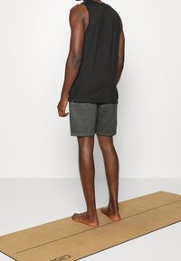 Débardeur noir sans manches et shorts gris, debout sur un tapis beige clair. Présente une texture lisse et une coupe décontractée.