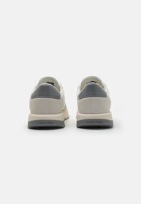 Grijze en witte sneakers met een bovenwerk van glad leer, suède accenten en een dikke zool. Heeft een logo op de achterkant. Minimalistisch ontwerp.
