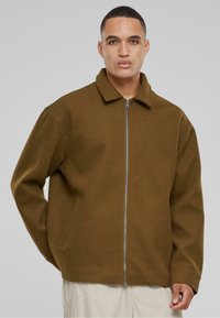 Brown zip-up jacket with a collar, made of soft, textured material. Features side pockets and a relaxed fit. Simple, minimal design.