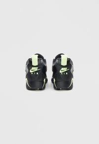 I sneakers neri Nike presentano un design testurizzato con un tassello sul tallone e dettagli in verde neon. La parte posteriore mostra il logo "AIR" in modo prominente.