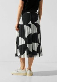 Plisserad midi kjol i genomskinligt tyg med ett djärvt svart-vitt mönster. Styld med en åtsittande svart topp och vita sneakers.