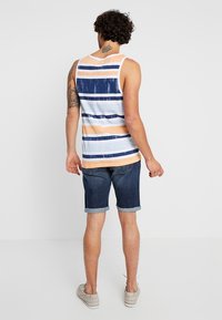 Pánské tílko s horizontálními pruhy v námořnické modré, broskvové a světle modré barvě. V kombinaci s tmavými denimovými šortkami s ohrnutými manžetami a plátěnými botami.