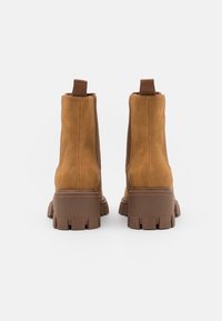 Stivaletti alla caviglia in suede marrone con suole in gomma spessa e linguette in tessuto. Presentano una superficie liscia e un design arrotondato.