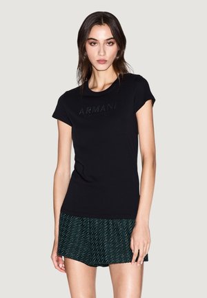 T-shirt en coton noir avec manches courtes et logo "Armani" en relief. Associé à une jupe verte texturée. Design simple et ajusté.