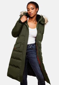 Long olive-green puffer coat with a fur-lined hood, zippered front, and multiple pockets. Features ribbed cuffs and red accents.